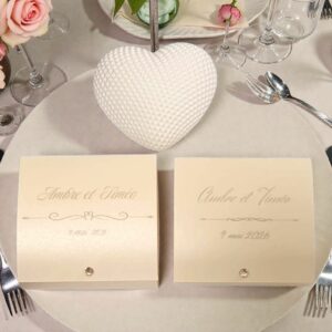 Boîtes à dragées mariage personnalisées avec cœur blanc texturé, présentées sur une table décorée de fleurs roses