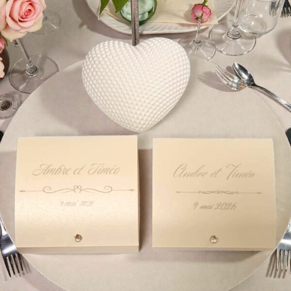 Boîtes à dragées mariage personnalisées avec cœur blanc texturé, présentées sur une table décorée de fleurs roses