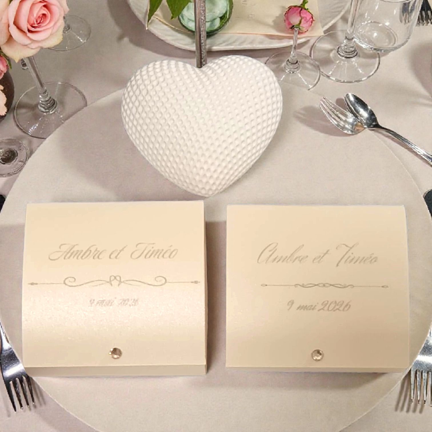 Boîtes à dragées mariage personnalisées avec cœur blanc texturé, présentées sur une table décorée de fleurs roses